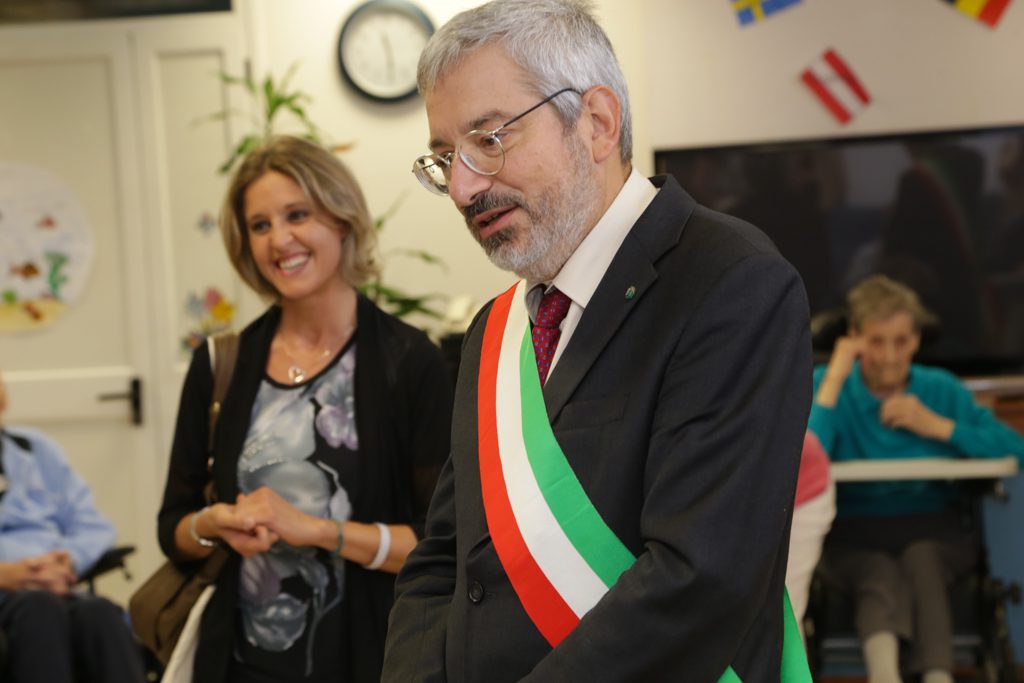 Un'immagine che ritrae occhiali, sorriso, cappotto, bandiera e cravatta.