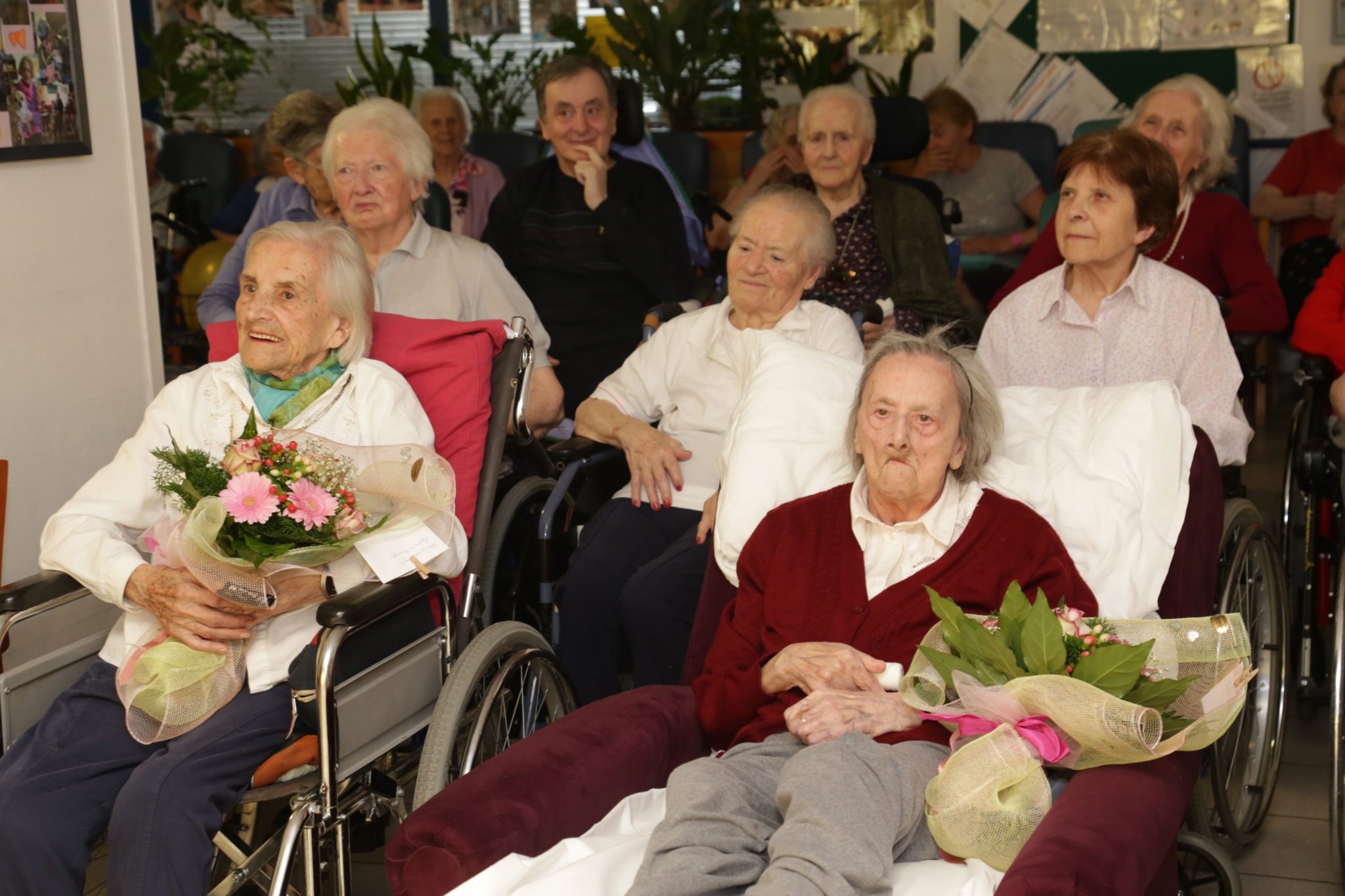 Un'immagine che ritrae sedia a rotelle, sedia, mobilia, casa di riposo e composizione floreale.
