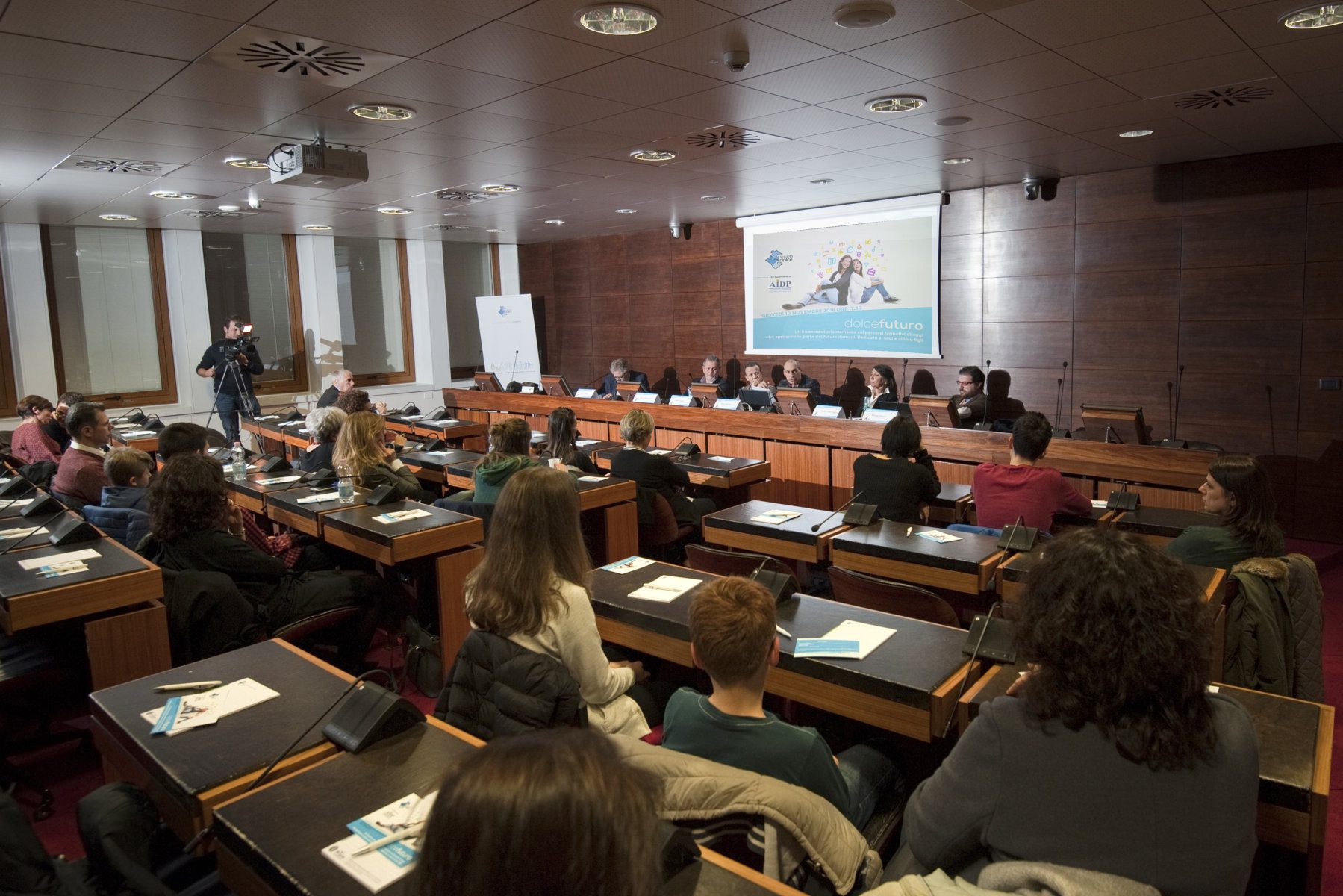 Un'immagine che ritrae mobilia, sedia, pubblico, sala e sala conferenze.
